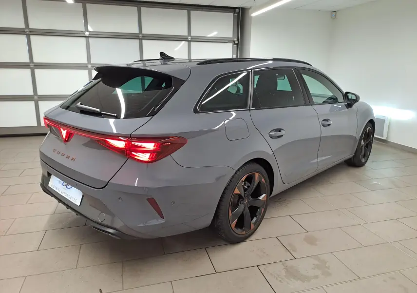 Vue 3/4 arrière droite d'une CUPRA Leon ST gris Graphène avec jantes cuivrées et toit ouvrant panoramique en intérieur showroom.