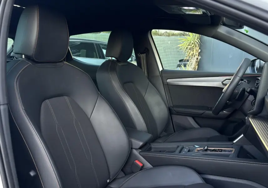 Vue intérieure côté droit des sièges avant noirs en cuir et tissu de la CUPRA Leon 2025 avec accoudoir central et volant Supersports.