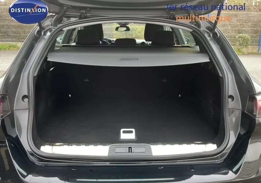Coffre ouvert vu de l'arrière d'une Peugeot 508 SW noire Perla Nera, espace de chargement spacieux et tapis noir.