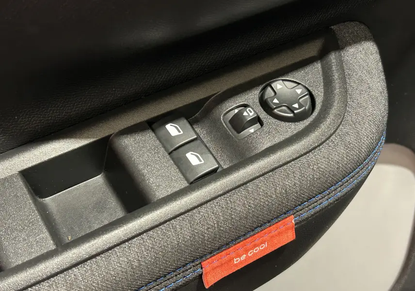 Gros plan sur les commandes de lève-vitres et rétroviseurs côté conducteur d’une Citroën C3 gris Artense avec couture bleue et étiquette "be cool".
