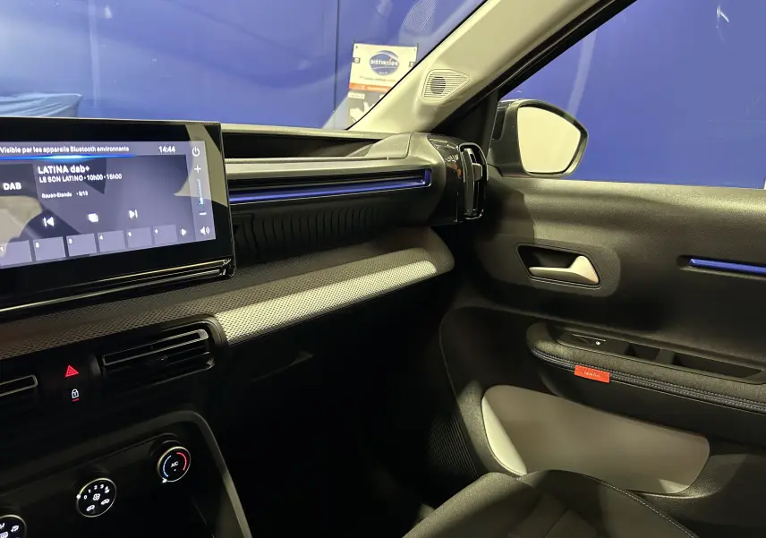 Vue intérieure côté passager de la Citroën C3 2025 gris Artense, avec tableau de bord moderne et éclairage bleu subtil.