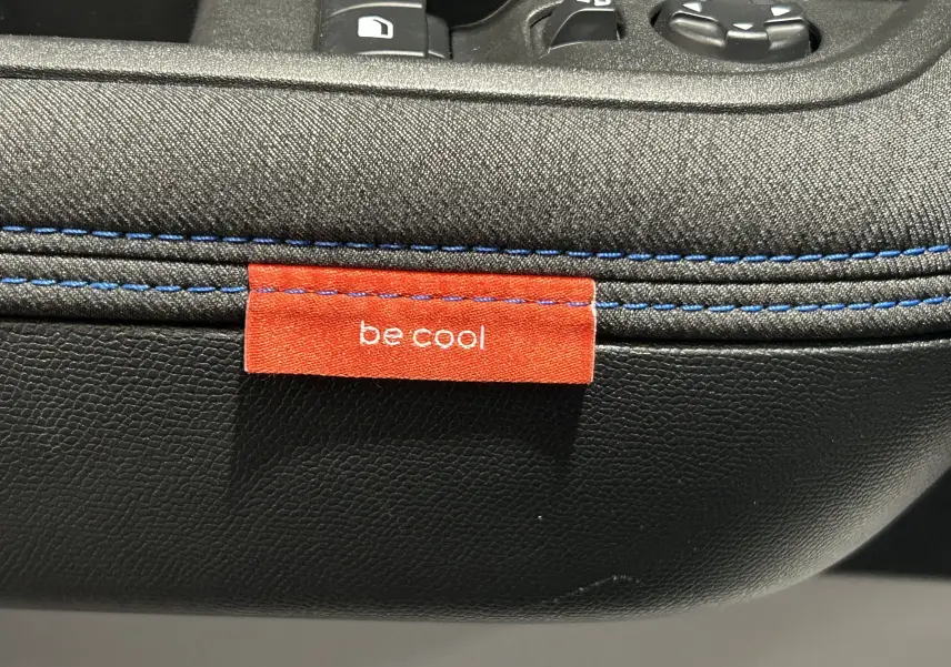Détail intérieur montrant une étiquette rouge "be cool" sur la sellerie noire avec surpiqûres bleues du Citroën C3 Gris Artense.