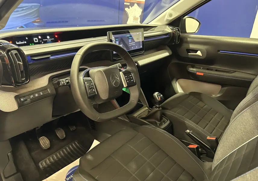 Vue intérieure côté conducteur de la Citroën C3 Turbo 100 Plus gris Artense, avec volant cuir et écran tactile central.