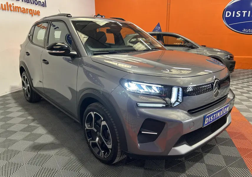Vue 3/4 avant d'une Citroën C3 Turbo 100 PLUS gris Artense avec phares LED allumés dans un showroom.