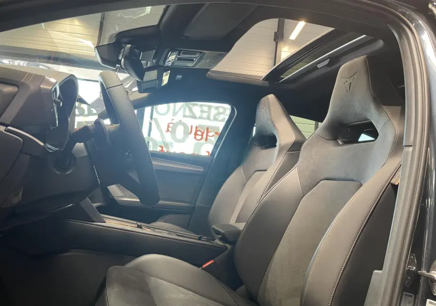 Vue intérieure côté conducteur de la CUPRA Leon 2026 gris, sièges baquets suédine noir avec surpiqûres cuivrées et toit panoramique.