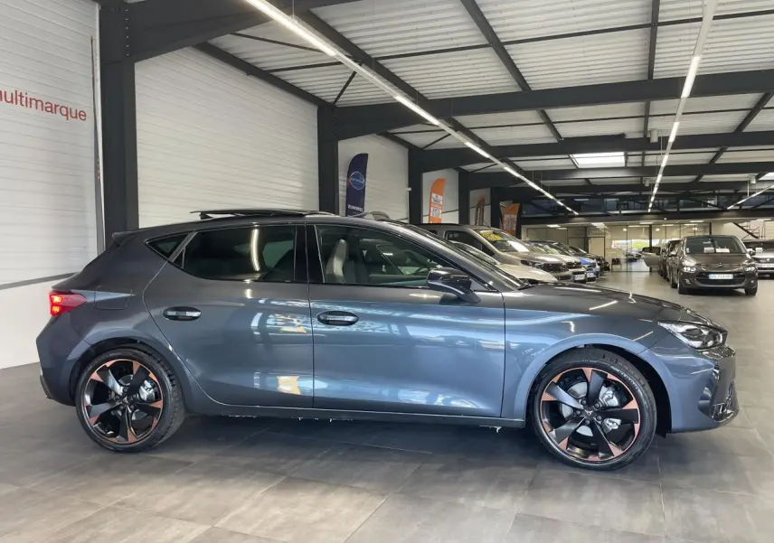 Vue de profil côté gauche d'une CUPRA Leon gris magnétique avec jantes alliage 18'' cuivrées en showroom.