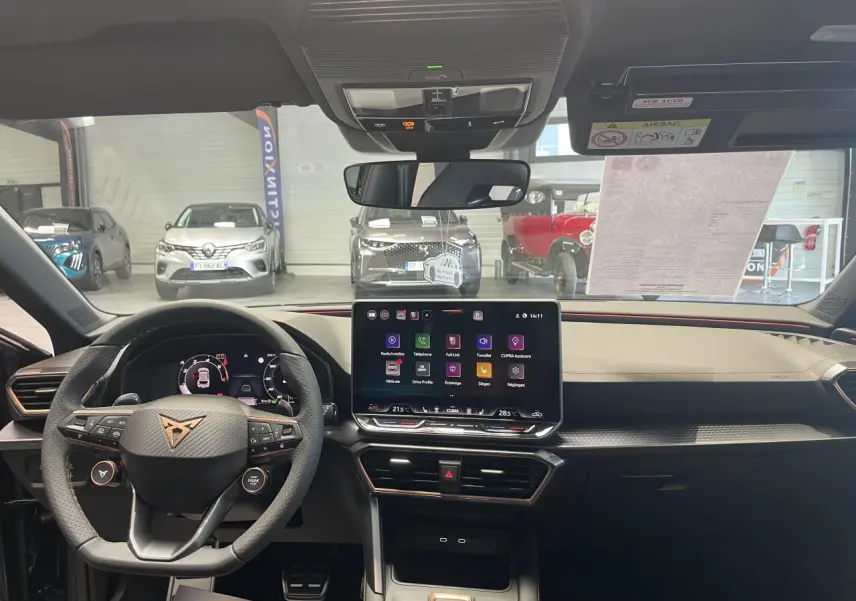 Vue intérieure avant du CUPRA Leon 2026 avec tableau de bord noir, écran tactile central et volant cuir à logo cuivré.