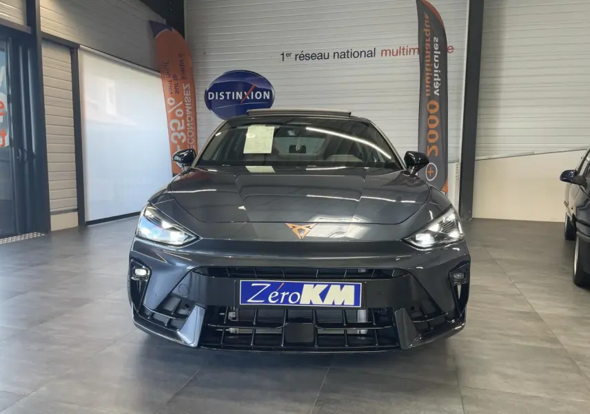 Vue de face d'une CUPRA Leon gris magnétique avec logo Cupra lumineux et plaques "Zero KM" en concession.