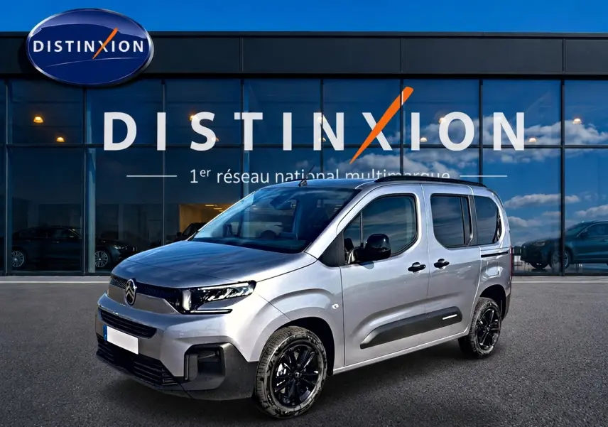 Citroën Berlingo Steel Grey vue 3/4 avant droit, avec jantes noires et barres de toit visibles devant vitrine Distinxion.
