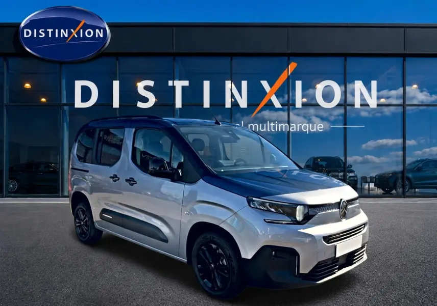 Vue 3/4 avant droit du Citroën Berlingo gris acier avec jantes noires, devant une vitrine Distinxion.