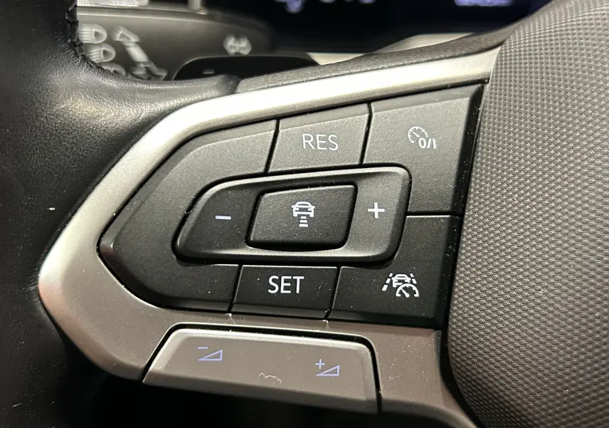 Gros plan sur les commandes du régulateur de vitesse au volant noir du Volkswagen Taigo blanc pur 2022.