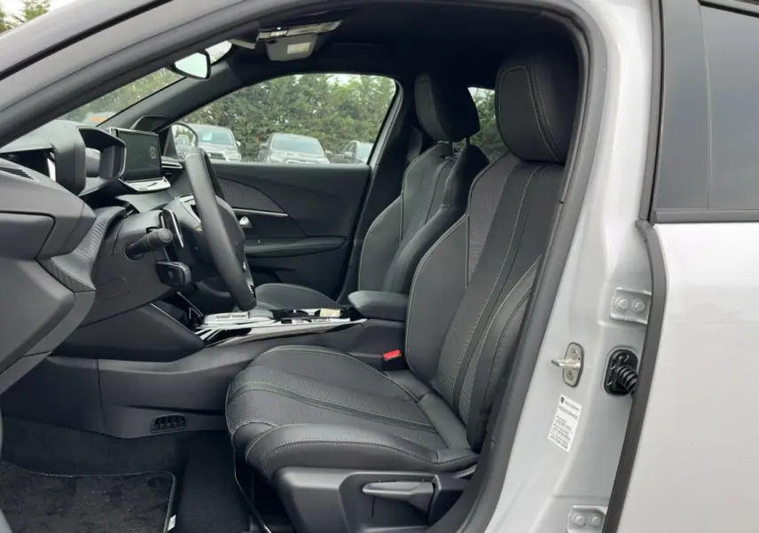 Vue intérieure côté conducteur du Peugeot 2008 Hybrid 145 GT Vision 2025 blanc okénite avec sièges sport noirs et surpiqûres vertes.