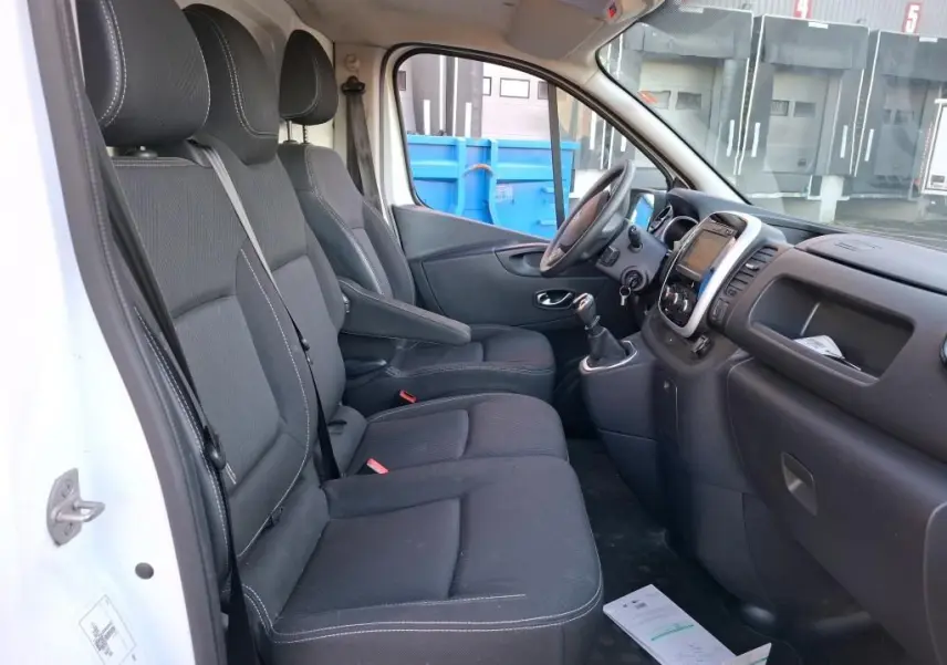 Intérieur du Renault Trafic Fourgon blanc 2019 vu côté conducteur, montrant sièges noirs et tableau de bord avec GPS intégré.