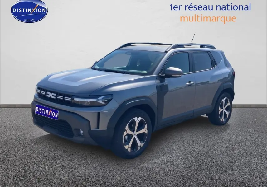 Dacia Duster gris schiste en 3/4 avant droit, avec jantes alliage et barres de toit visibles.