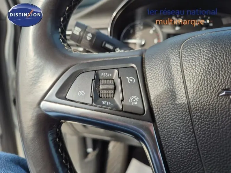 Gros plan sur les commandes de régulateur de vitesse au volant cuir noir d'un Opel Mokka X gris Minéral.