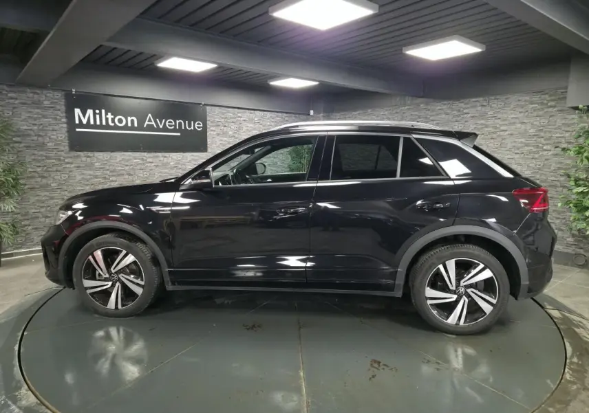 Profil droit d’un Volkswagen T-Roc noir 2023 R-Line avec jantes alliage et vitres arrière surteintées dans un showroom.