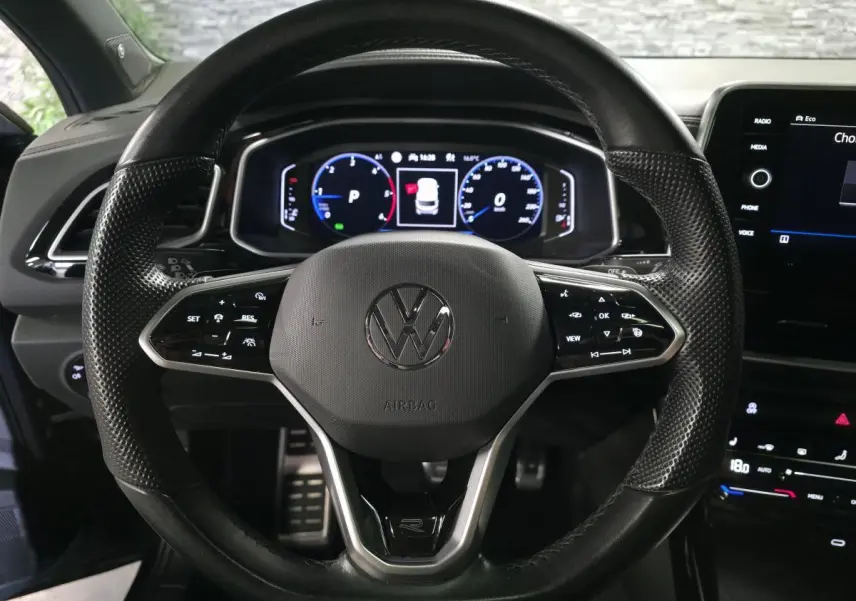 Vue rapprochée du volant en cuir noir avec logo Volkswagen et tableau de bord digital du T-Roc 2023.