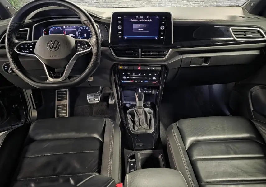 Vue intérieure avant du Volkswagen T-Roc 2.0 TDI noir, mettant en valeur le volant multifonction, l’écran tactile et la sellerie cuir R-Line.