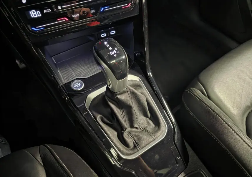 Gros plan sur la console centrale noire du Volkswagen T-Roc 2023 avec levier de vitesse automatique et sièges en cuir.