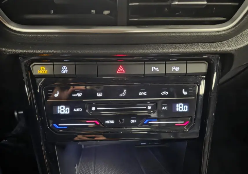 Vue rapprochée de la console centrale noire du Volkswagen T-Roc 2023 avec commandes de climatisation digitale et boutons de sécurité.
