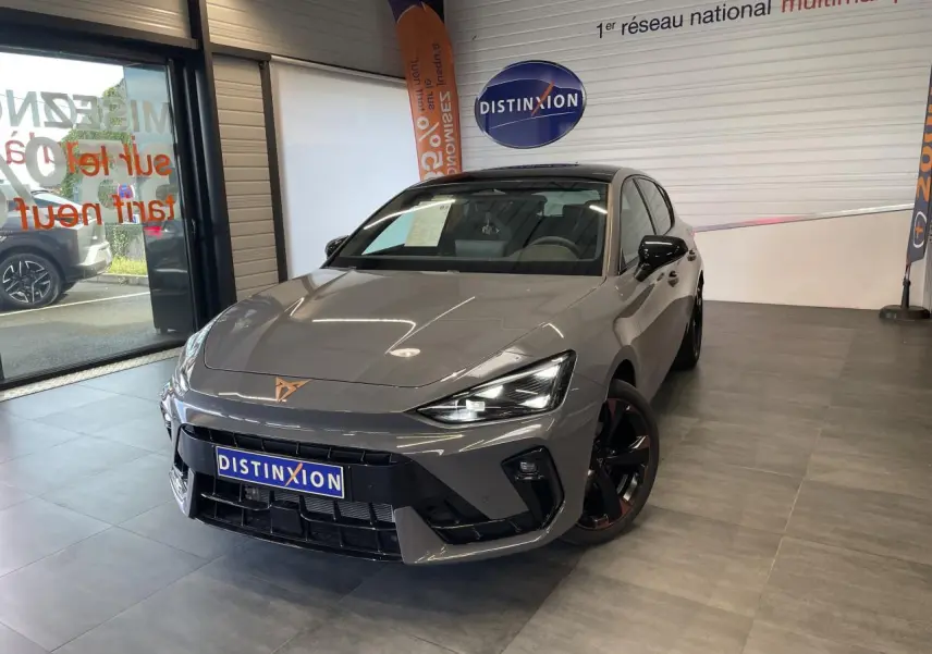 Vue 3/4 avant d'une CUPRA Leon gris magnétique avec jantes cuivrées et logo CUPRA sur le capot, en showroom.