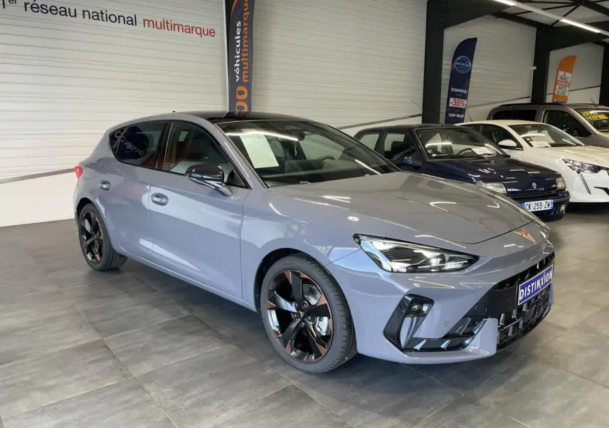 Vue 3/4 avant d'une CUPRA Leon gris magnétique avec jantes alliage noires et cuivrées en showroom.