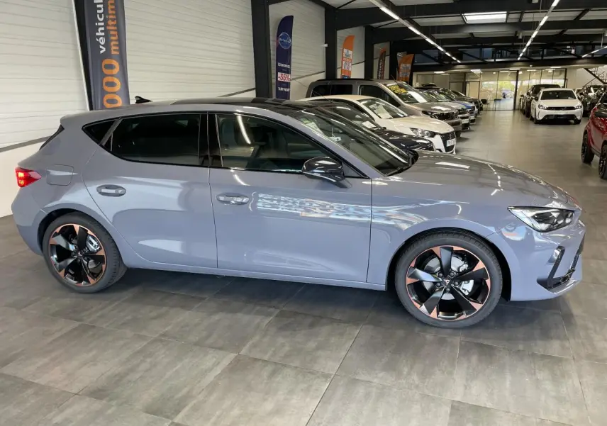 Vue de profil côté gauche d'une CUPRA Leon gris magnétique avec jantes alliage noires et cuivrées en showroom.