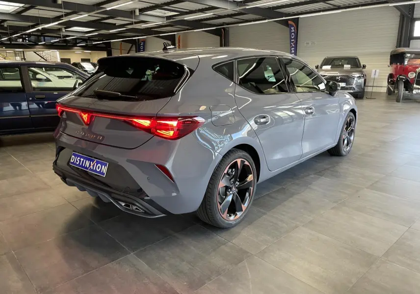 Vue 3/4 arrière droite d'une CUPRA Leon gris magnétique avec jantes alliage 18'' cuivrées et feux arrière Tri-LED allumés.