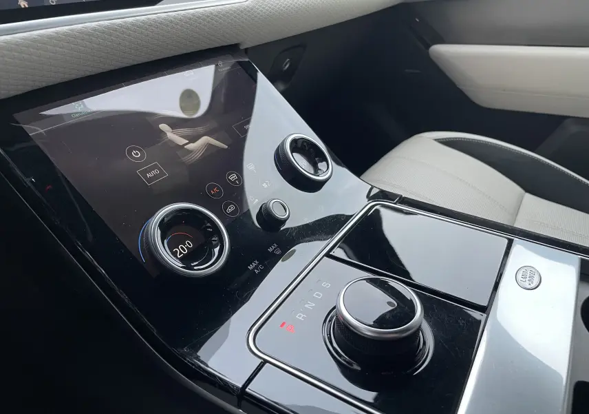 Gros plan sur la console centrale noire brillante du Range Rover Velar 2018 avec commandes tactiles et siège beige visible.