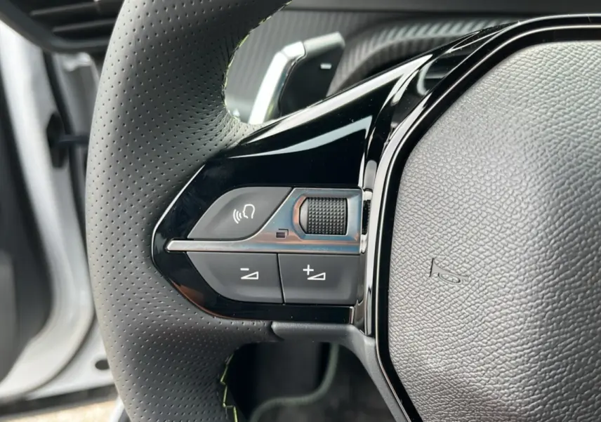 Gros plan sur les commandes à gauche du volant perforé du Peugeot 2008 Hybrid 145 GT Vision blanc okénite 2025.