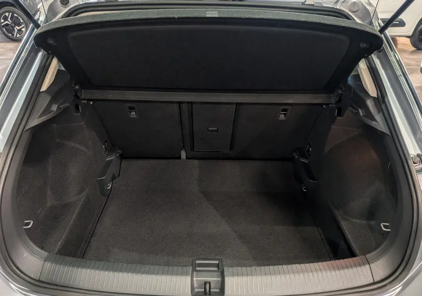 Coffre ouvert vu de l'arrière d'un Volkswagen T-Roc gris pyrite, montrant un espace de chargement propre et spacieux.