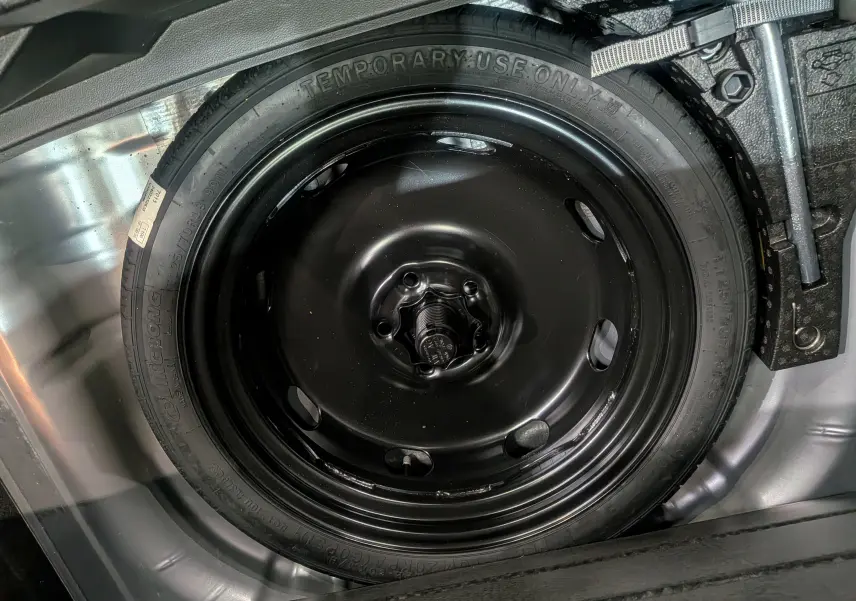 Gros plan sur la roue de secours noire dans le coffre d'un Volkswagen T-Roc gris pyrite 2024.