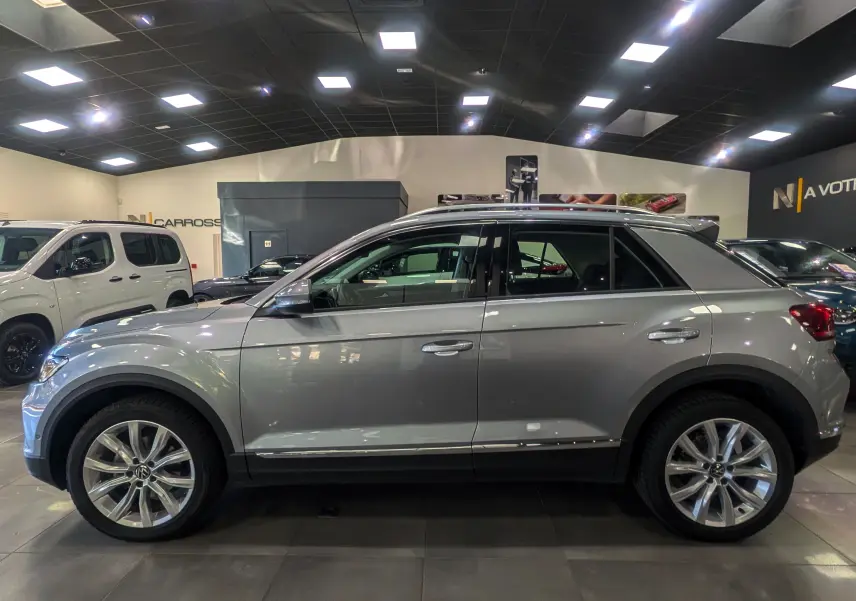 Profil droit du Volkswagen T-Roc 1.5 TSI gris pyrite 2024 en intérieur, avec jantes alliage et lignes épurées.