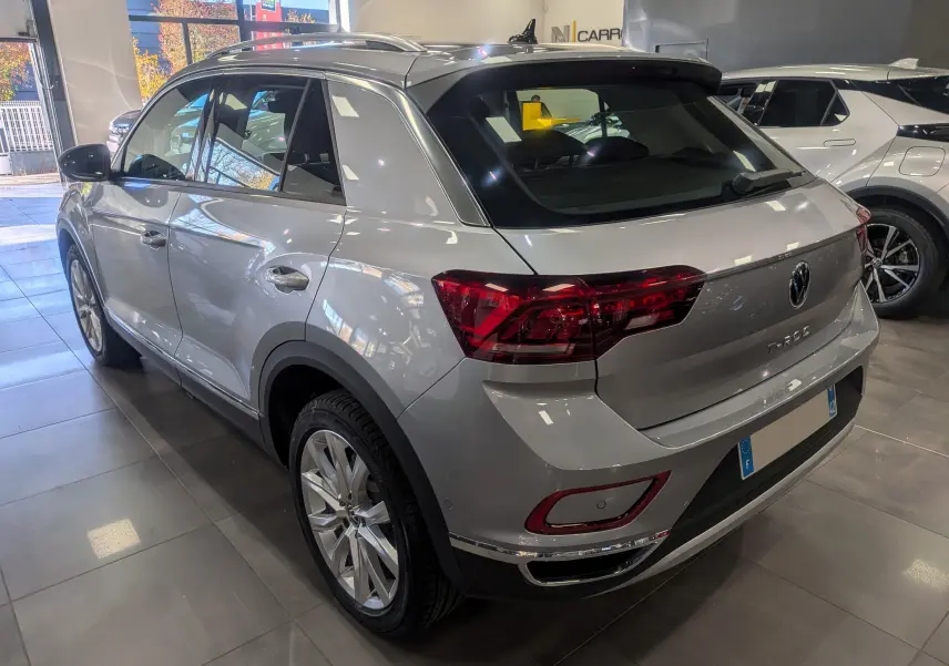 Volkswagen T-Roc gris pyrite vue 3/4 arrière droit en showroom, avec jantes alliage et feux arrière LED distinctifs.