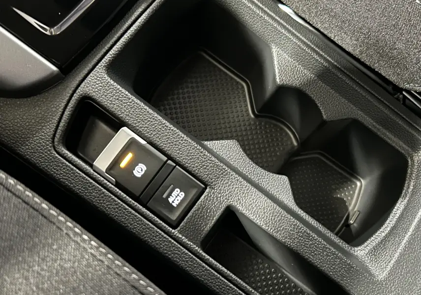 Gros plan sur la console centrale noire du Volkswagen T-Roc 2025, avec bouton frein à main électronique et porte-gobelets.