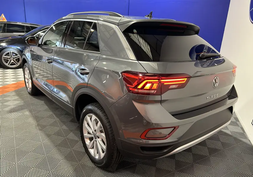 Vue 3/4 arrière droite du Volkswagen T-Roc gris Indium Metal 2025 avec feux arrière allumés dans un showroom.
