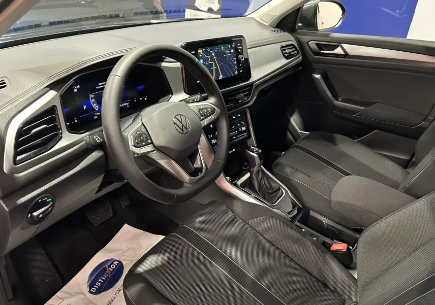 Vue intérieure côté conducteur du Volkswagen T-Roc 2025, avec tableau de bord numérique et sellerie tissu noire.