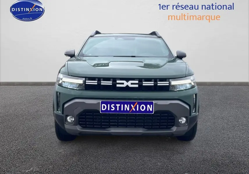 Vue frontale d'un Dacia Duster 2026 vert kaki avec calandre noire et phares LED allumés sur fond neutre.