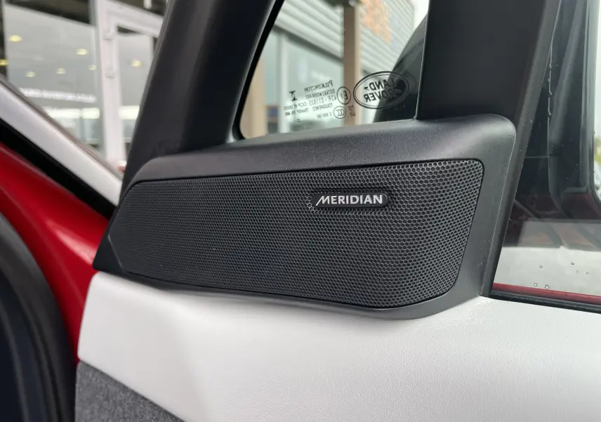 Gros plan sur l'enceinte Meridian intégrée à la porte côté gauche d'un Range Rover Sport P440 HSE R-Dynamic rouge italien.