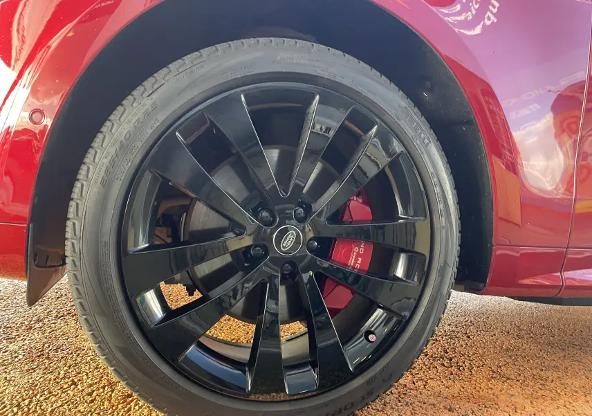 Gros plan sur la roue avant droite du Range Rover Sport P440 HSE R-Dynamic rouge Italian Racing avec jante alu noire 23 pouces.