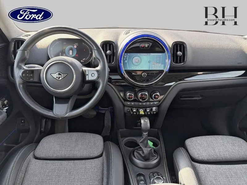 Vue intérieure avant du tableau de bord et volant noir avec écran central rond éclairé d'un MINI Countryman Cooper SE Moonwalk Grey 2021.