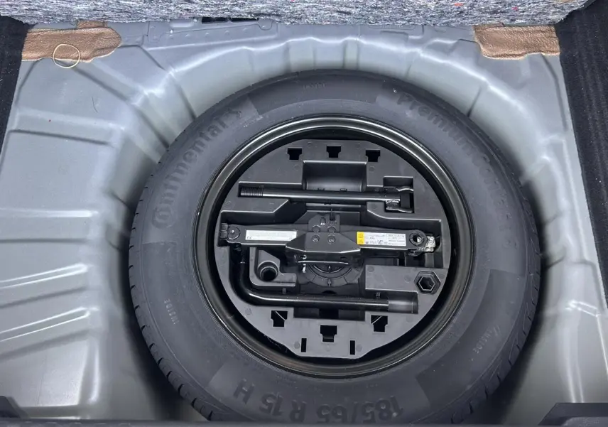 Vue plongeante sur la roue de secours tôle noire et son kit d'outils dans le coffre de la Renault Clio Noir Étoilé 2025.
