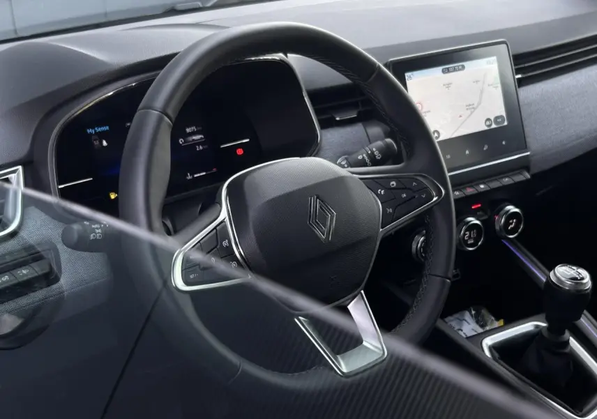 Vue intérieure côté conducteur de la Renault Clio noire étoilé 2025, volant multifonction et écran tactile central visibles.