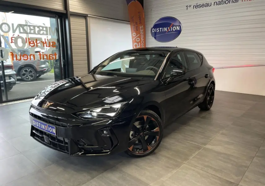 Vue 3/4 avant droite d'une CUPRA Leon noire avec jantes alliage noires et cuivrées, dans un showroom intérieur.