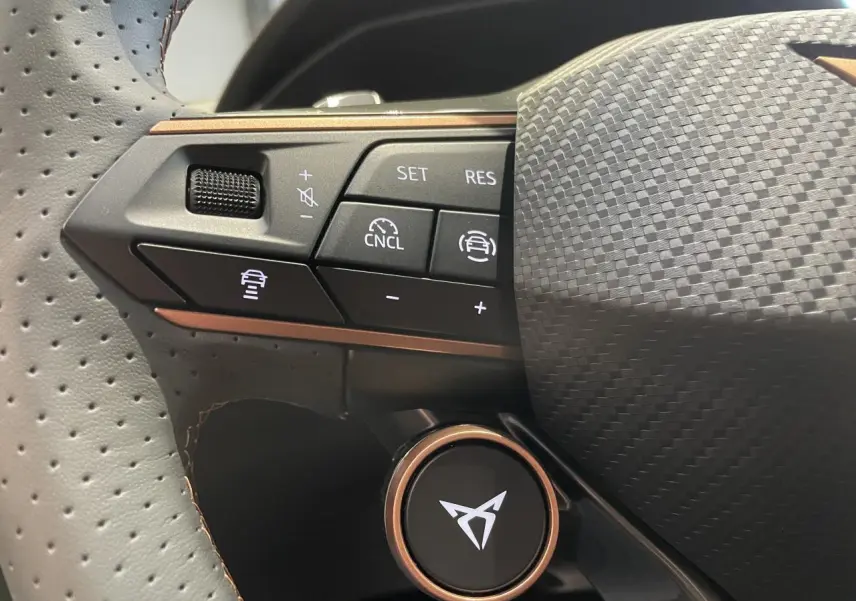 Gros plan sur le volant perforé noir avec boutons de commande et logo CUPRA cuivré au centre.