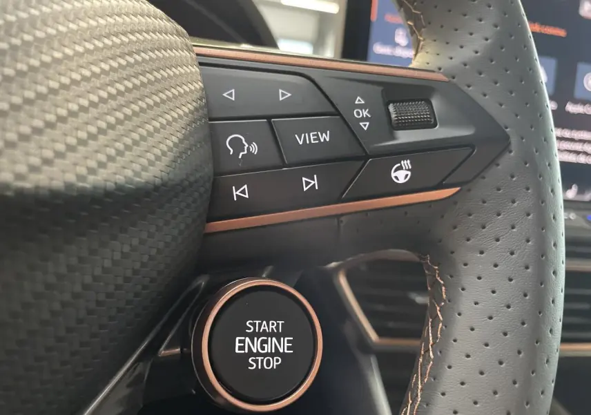 Gros plan sur le volant perforé noir avec surpiqûres cuivrées et bouton Start Engine Stop de la CUPRA Leon 2026.