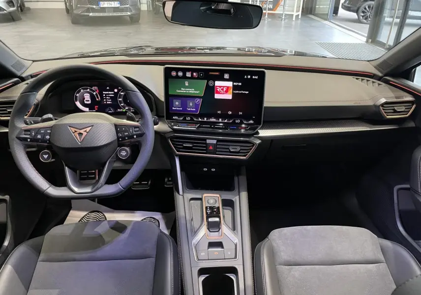 Vue intérieure avant de la CUPRA Leon 2026, tableau de bord noir avec volant sport et écran tactile central.