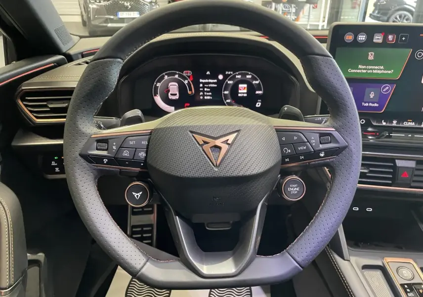Vue rapprochée du volant cuir perforé noir avec logo Cupra cuivré et tableau de bord digital lumineux.