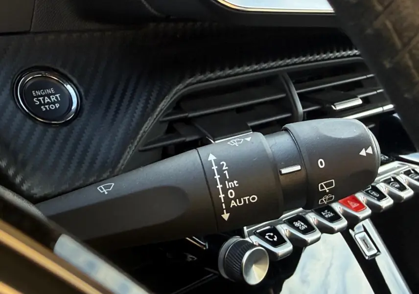 Gros plan sur le commodo d’essuie-glace et le bouton start/stop dans l’habitacle noir du Peugeot e-2008 2025.