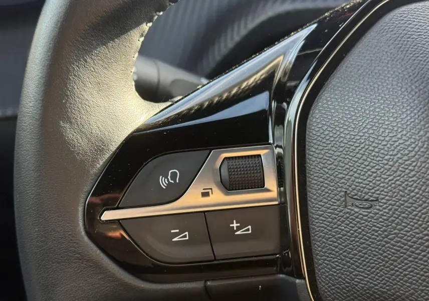Gros plan sur les commandes gauche du volant noir du Peugeot e-2008 2025, avec boutons de volume et commande vocale.